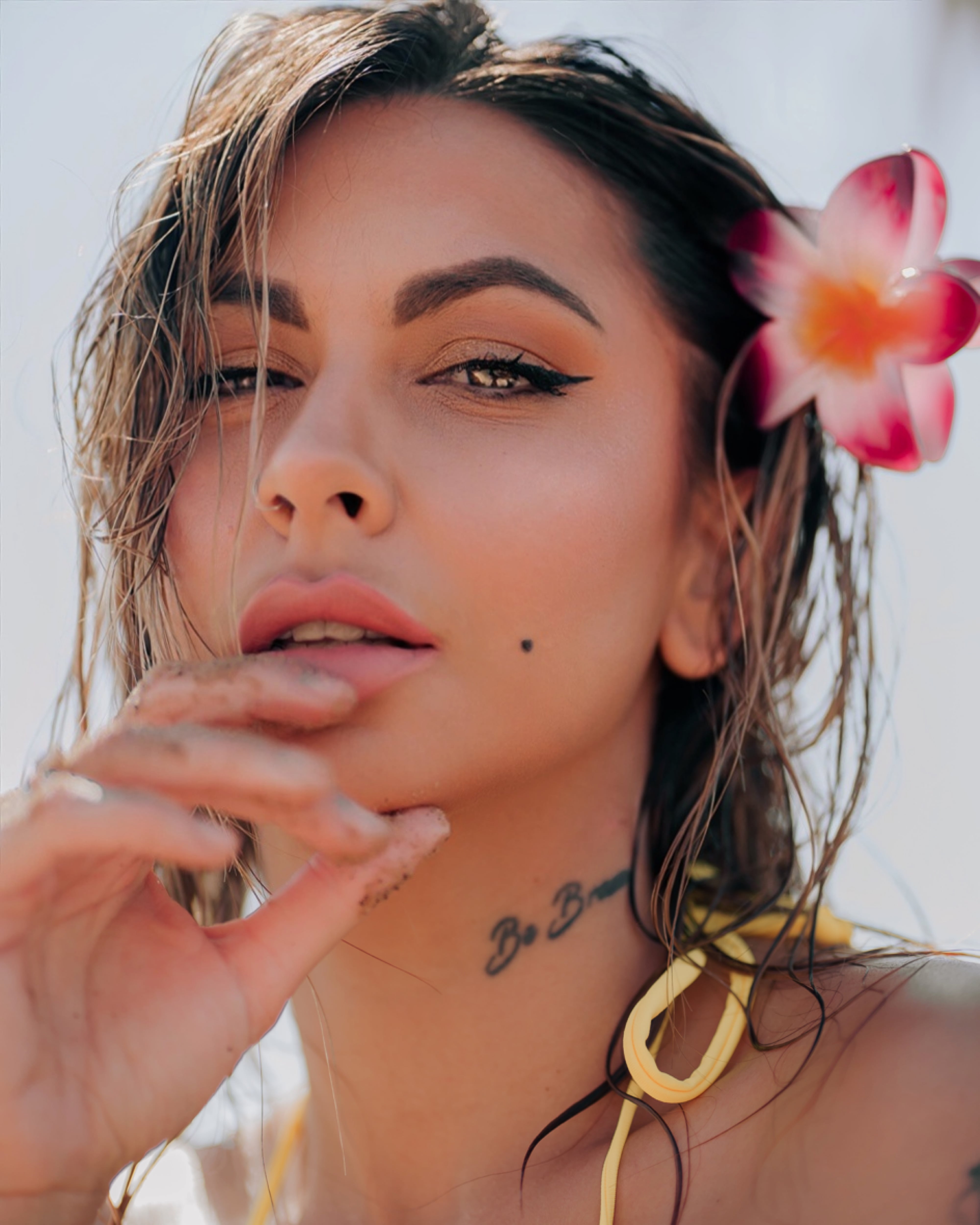 Retrato cercano de una mujer con una mano junto a la barbilla y una flor en el pelo